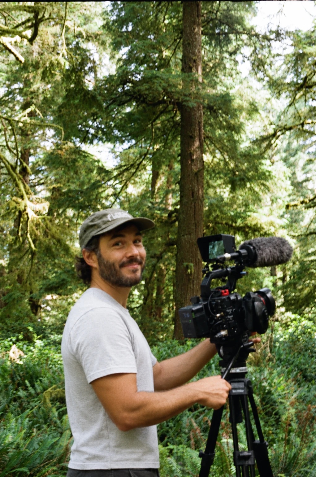 Andrew Tomayko smiling beside his camera in an old-growth forest